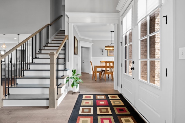 foyer entrance featuring a wainscoted wall, wood finished floors, stairs, and crown molding