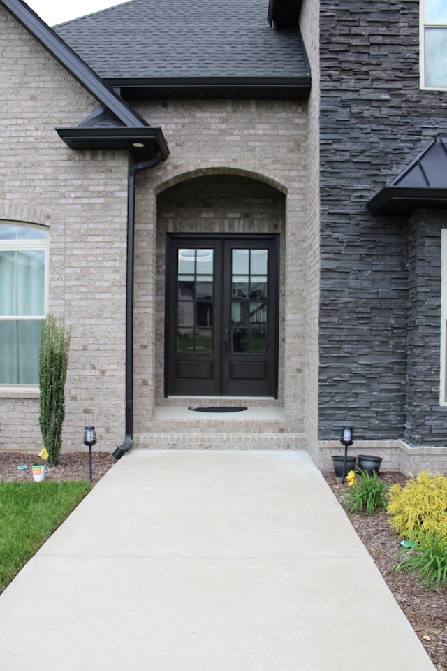 doorway to property with french doors, roof with shingles, and brick siding