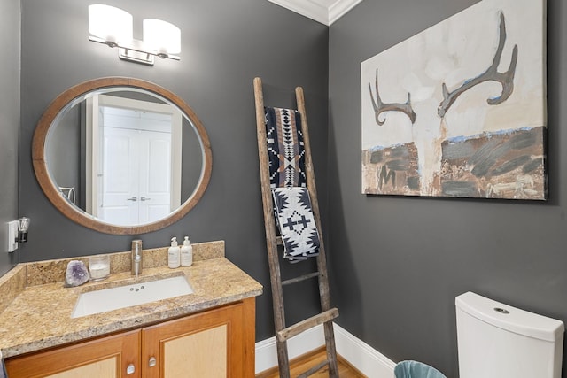 half bath featuring toilet, baseboards, ornamental molding, and vanity