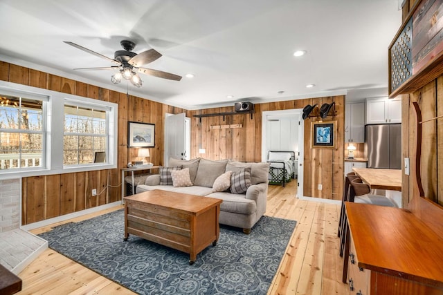 living area featuring light wood finished floors, wood walls, and a ceiling fan