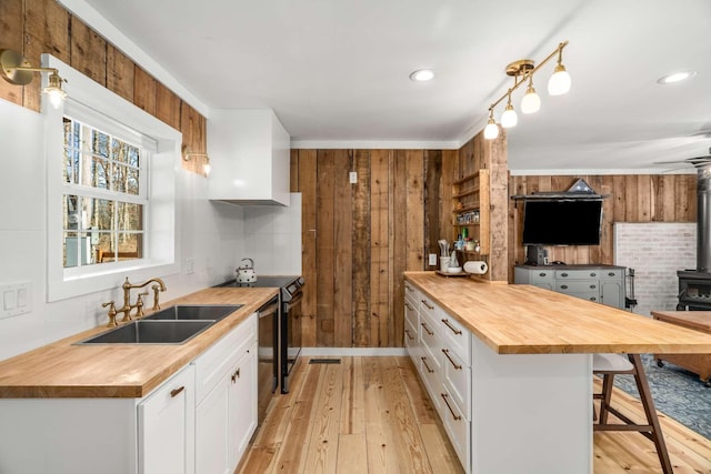 kitchen with electric range, butcher block countertops, open floor plan, a wood stove, and a sink