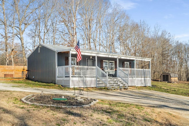 view of front of home featuring an outbuilding, a porch, a storage shed, fence, and driveway