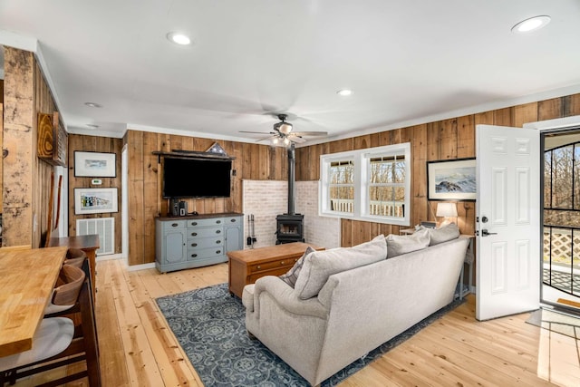 living area with a wood stove, a healthy amount of sunlight, light wood-style flooring, and visible vents