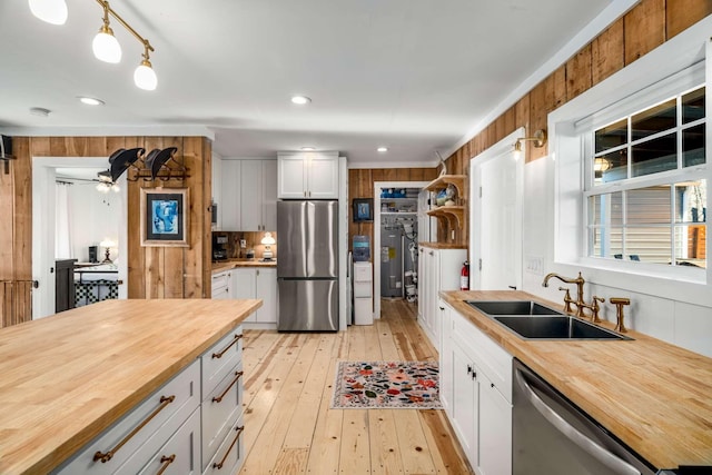 kitchen featuring wooden walls, stainless steel appliances, butcher block counters, a sink, and light wood-type flooring