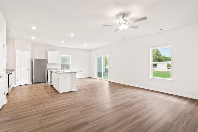 kitchen with a sink, white cabinets, open floor plan, appliances with stainless steel finishes, and light wood finished floors