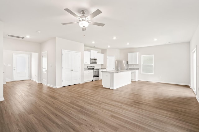 kitchen featuring visible vents, appliances with stainless steel finishes, open floor plan, an island with sink, and light wood-type flooring