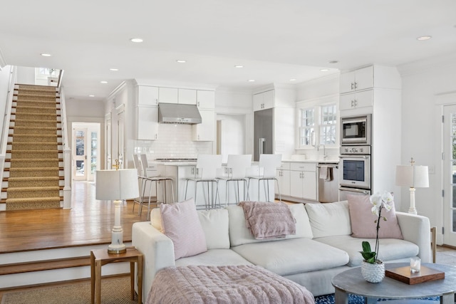 living room featuring stairs, ornamental molding, light wood-style floors, and recessed lighting