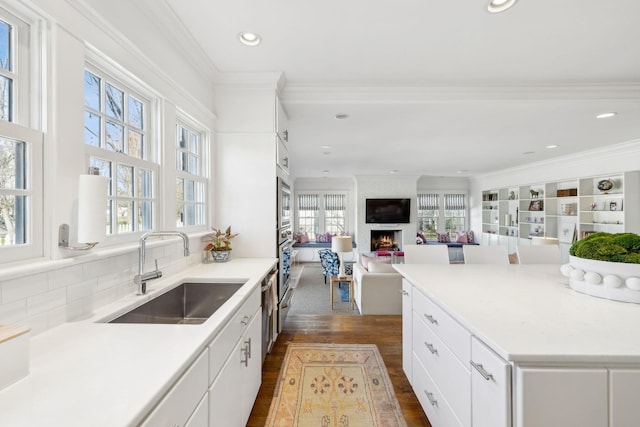 kitchen with a fireplace, a sink, white cabinetry, dark wood-style floors, and crown molding