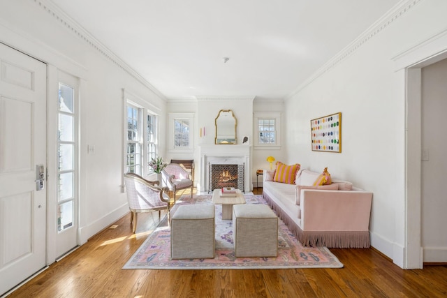 living room featuring baseboards, a lit fireplace, wood finished floors, and crown molding