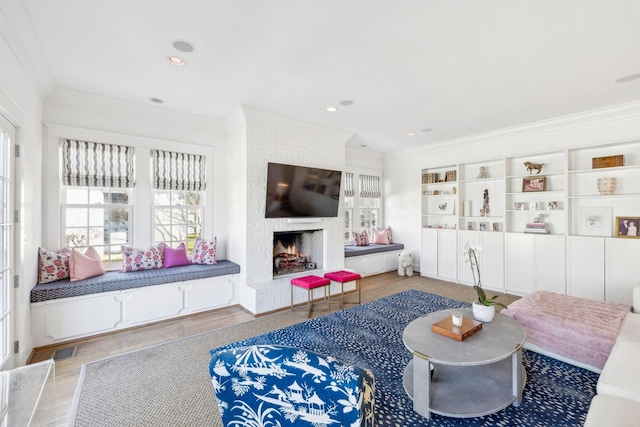 living area with visible vents, ornamental molding, wood finished floors, a brick fireplace, and recessed lighting