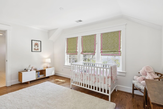 bedroom with lofted ceiling, visible vents, wood finished floors, a crib, and baseboards