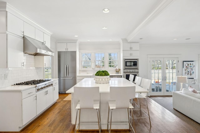 kitchen featuring decorative backsplash, a kitchen breakfast bar, wood finished floors, stainless steel appliances, and under cabinet range hood