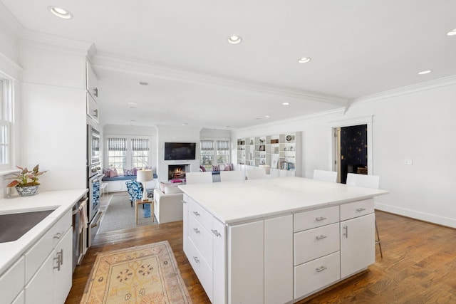 kitchen featuring a large fireplace, dark wood-style floors, white cabinets, and ornamental molding