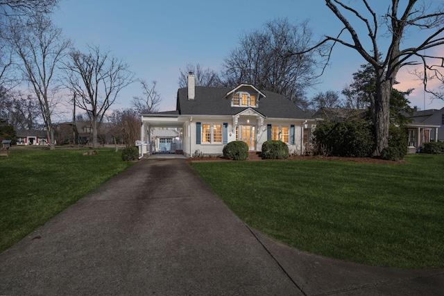 view of front facade featuring aphalt driveway, a chimney, a front lawn, and an attached carport