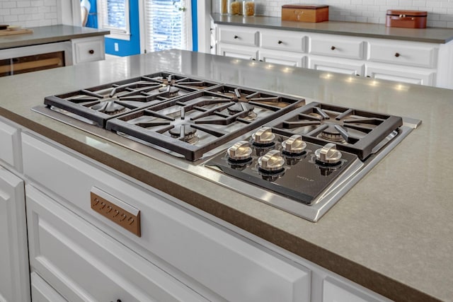 room details with dark countertops, white cabinets, stainless steel gas stovetop, and backsplash