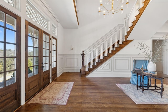 foyer featuring french doors, a decorative wall, an inviting chandelier, wood finished floors, and stairs