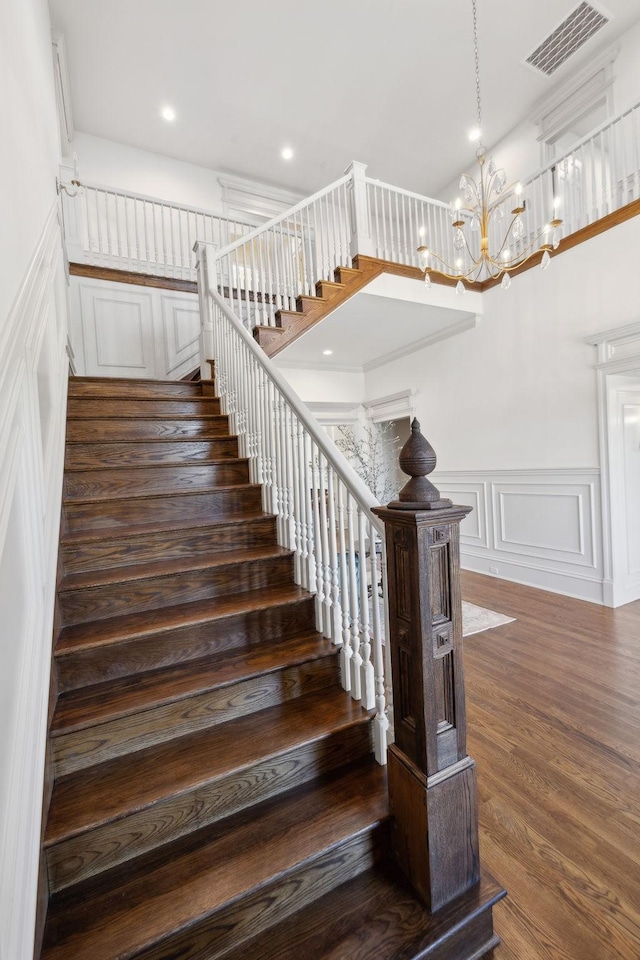 stairway featuring a wainscoted wall, visible vents, a decorative wall, wood finished floors, and a chandelier