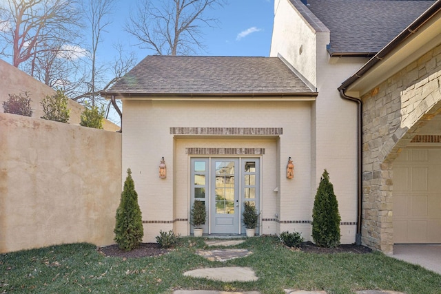 entrance to property featuring french doors, roof with shingles, and brick siding