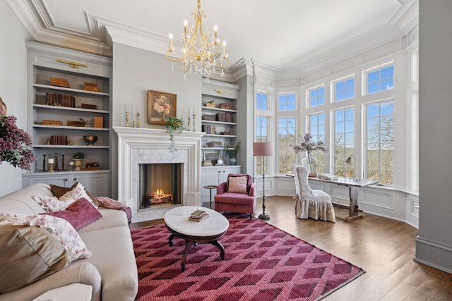 sitting room featuring built in shelves, a decorative wall, ornamental molding, a high end fireplace, and wood finished floors