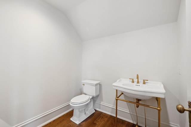 bathroom with lofted ceiling, toilet, a sink, wood finished floors, and baseboards