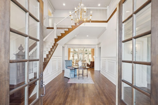 entryway with dark wood-style flooring, a notable chandelier, a decorative wall, and stairs