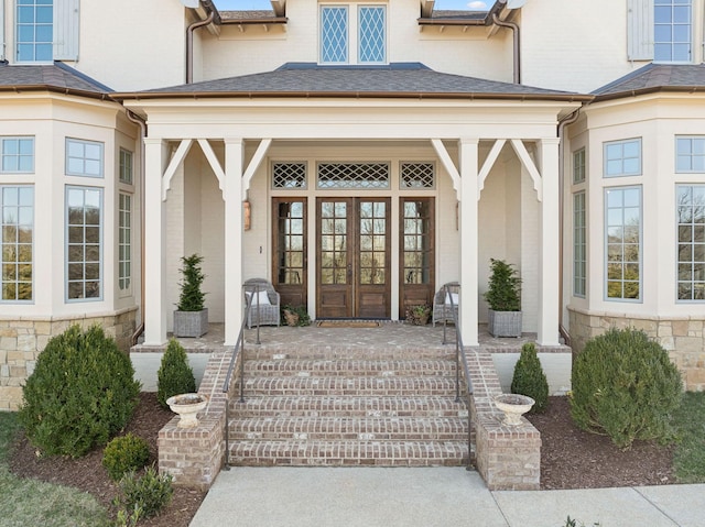 view of exterior entry with stone siding, roof with shingles, and french doors