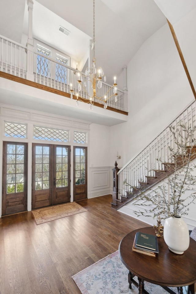 foyer with a decorative wall, a high ceiling, wood finished floors, stairway, and an inviting chandelier