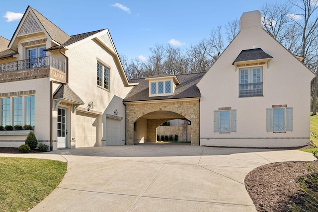 view of front of property featuring driveway, a shingled roof, stone siding, and a balcony