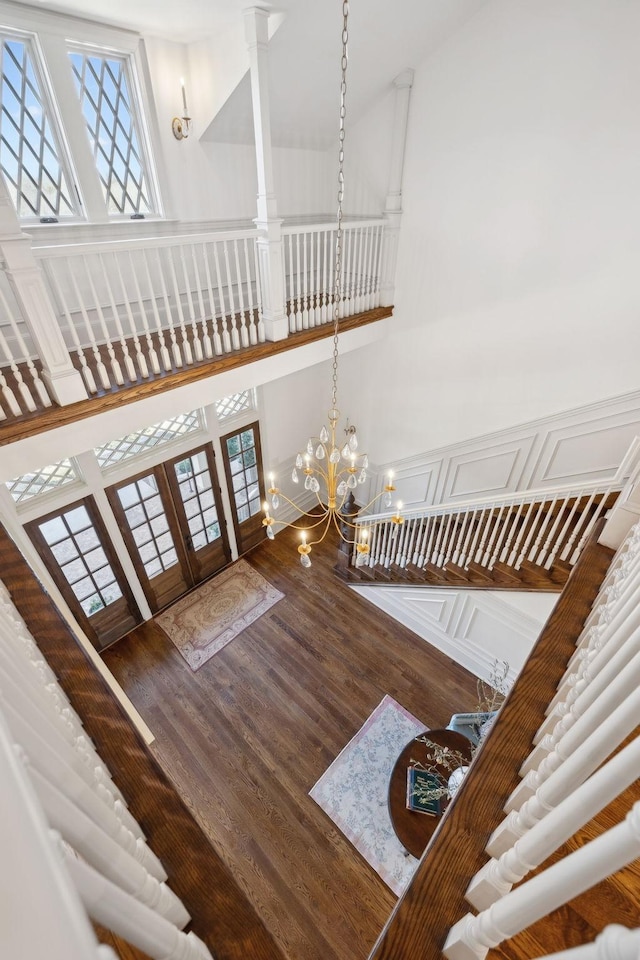 entryway featuring wood finished floors, a towering ceiling, french doors, an inviting chandelier, and ornate columns