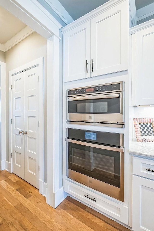 room details featuring white cabinets, crown molding, stainless steel double oven, light wood-type flooring, and backsplash