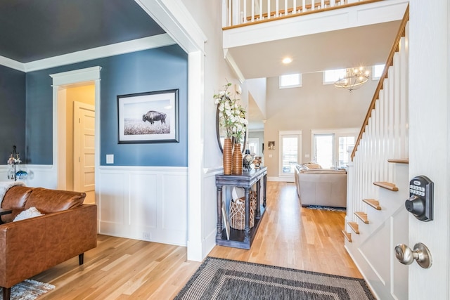 entrance foyer with a wainscoted wall, ornamental molding, stairway, and wood finished floors