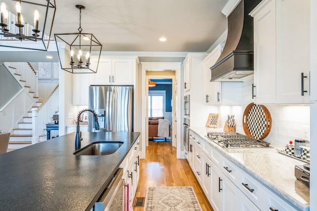 kitchen with stainless steel appliances, premium range hood, a sink, white cabinetry, and light wood finished floors