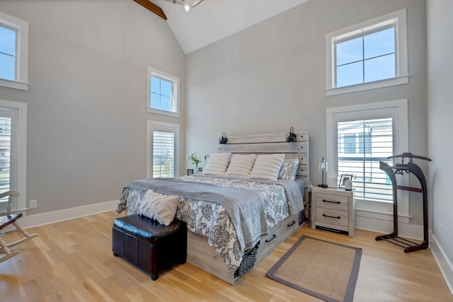 bedroom featuring high vaulted ceiling, light wood-type flooring, and baseboards