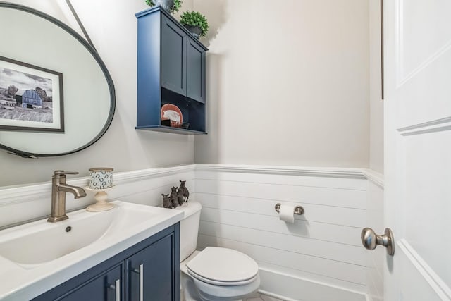 half bathroom featuring toilet, a wainscoted wall, and vanity