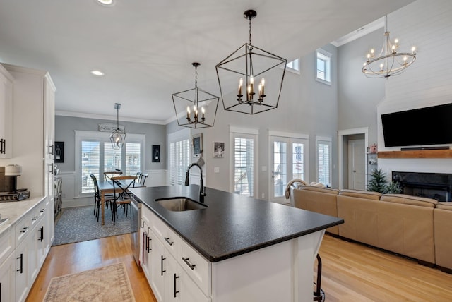 kitchen with a center island with sink, ornamental molding, light wood-style floors, a sink, and dishwasher