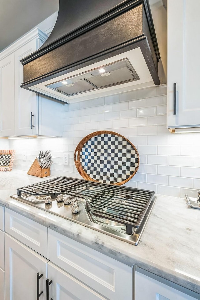 room details featuring tasteful backsplash, light stone counters, stainless steel gas stovetop, white cabinetry, and exhaust hood