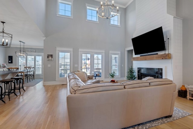 living area with a notable chandelier, baseboards, light wood-style floors, ornamental molding, and a glass covered fireplace