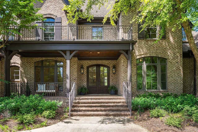 view of exterior entry featuring french doors, a balcony, and brick siding