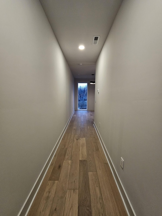 hall with wood finished floors, visible vents, and baseboards