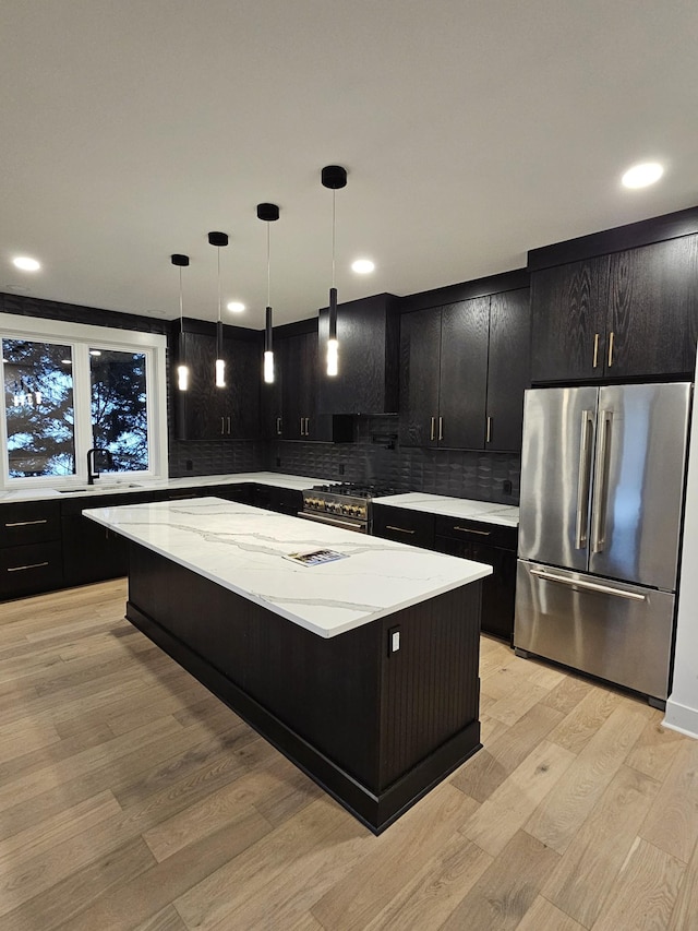 kitchen with a kitchen island, appliances with stainless steel finishes, dark cabinetry, light wood-style floors, and exhaust hood