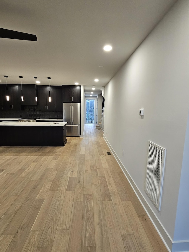 kitchen with light wood finished floors, stainless steel fridge, visible vents, light countertops, and dark cabinetry