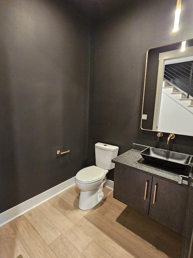 half bathroom featuring baseboards, vanity, toilet, and wood finished floors