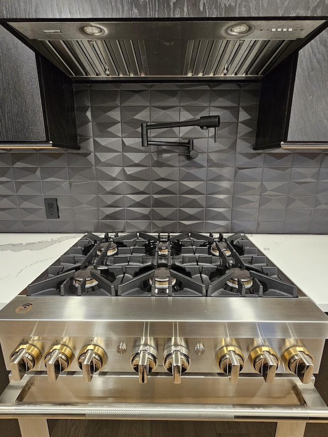 room details with gas stove, range hood, decorative backsplash, and light stone countertops