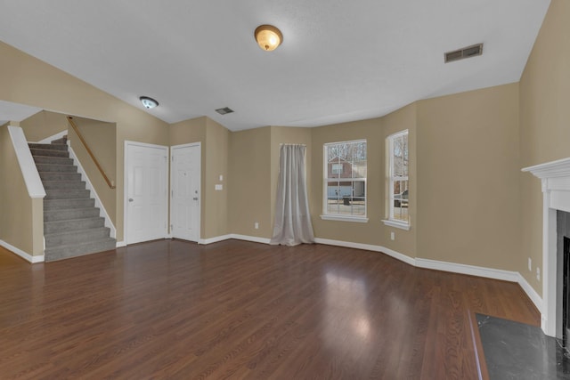 unfurnished living room featuring a fireplace, visible vents, wood finished floors, baseboards, and stairs