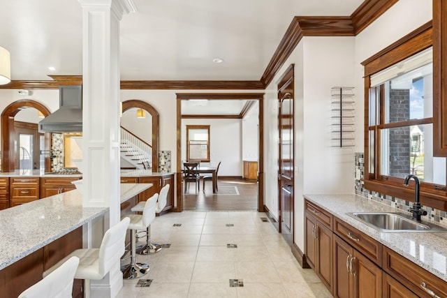 kitchen featuring a healthy amount of sunlight, wall chimney exhaust hood, decorative columns, and a sink