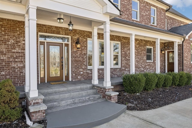 doorway to property with covered porch and brick siding