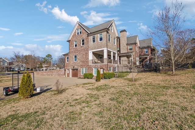 back of house with driveway, a garage, a lawn, a chimney, and brick siding