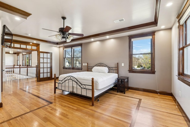 bedroom featuring visible vents, baseboards, ornamental molding, a tray ceiling, and light wood-style floors