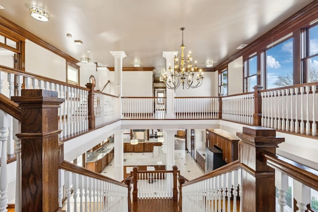 staircase with ornate columns, a high ceiling, a chandelier, and crown molding