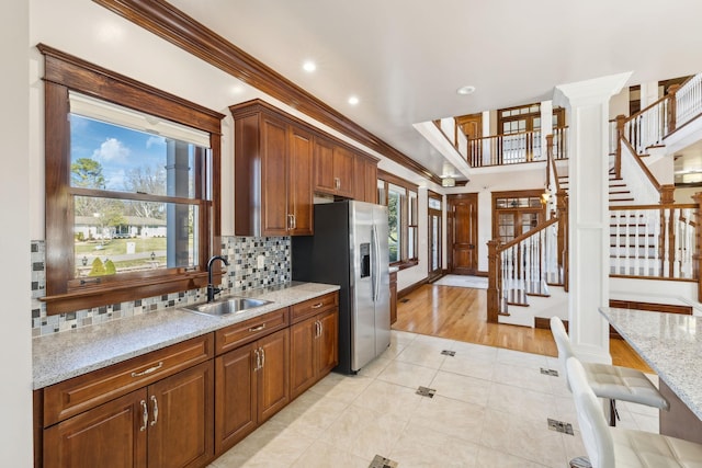 kitchen with light tile patterned flooring, a sink, stainless steel fridge with ice dispenser, ornamental molding, and decorative backsplash